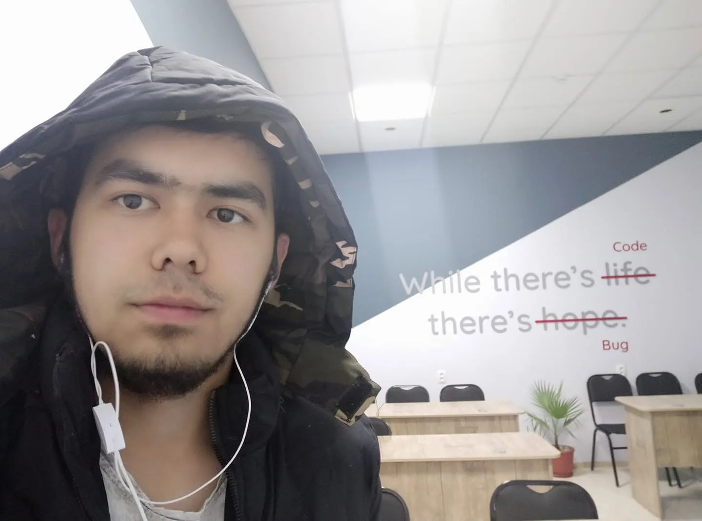 selfie in a classroom with “while there’s code, there’s bug” on the wall